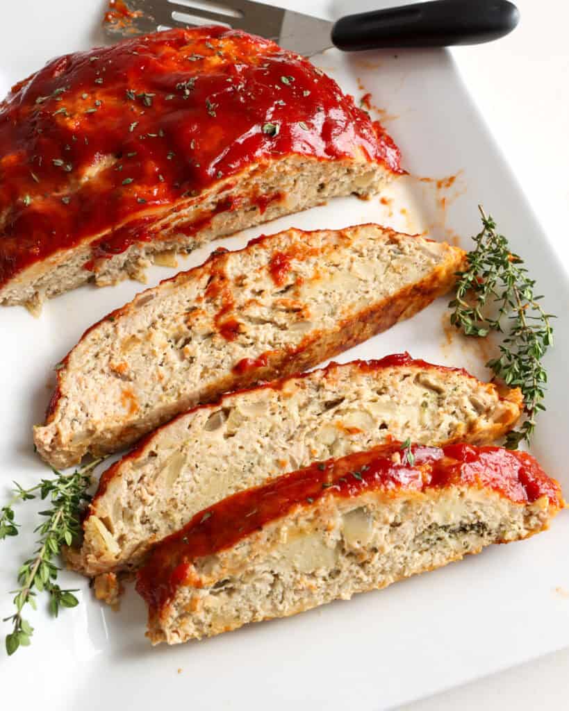 Slices of glazed chicken meatloaf on a serving platter with fresh thyme.