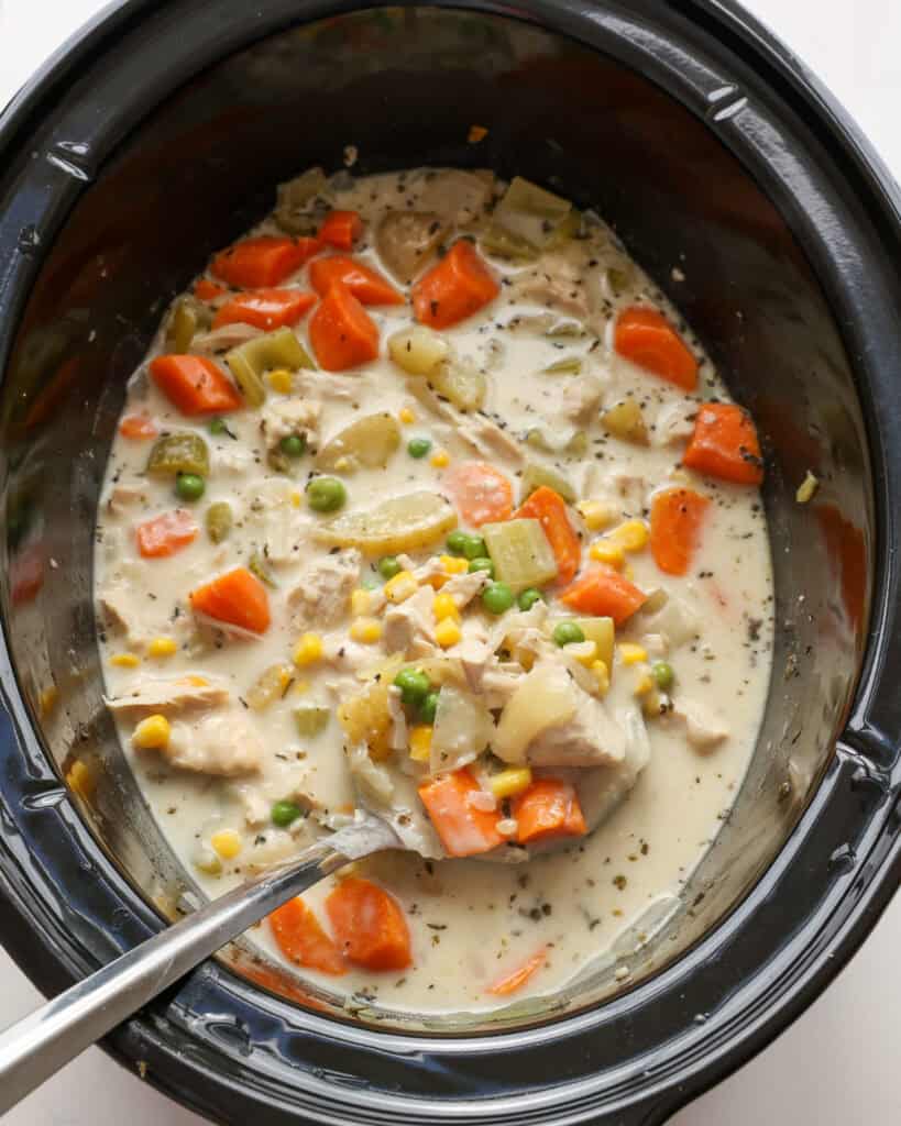 A crock pot full chicken strew with potatoes, carrots, peas, and corn. 