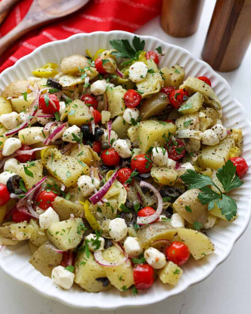 A close up view of Italian potato salad with black olives, tomatoes, artichoke hearts, and capers.