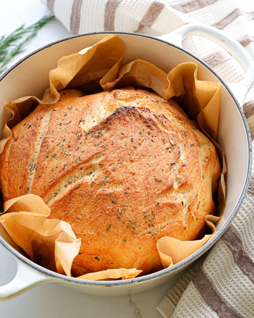 A loaf of goilden brown potato bread on parchment paper in a Dutch oven.