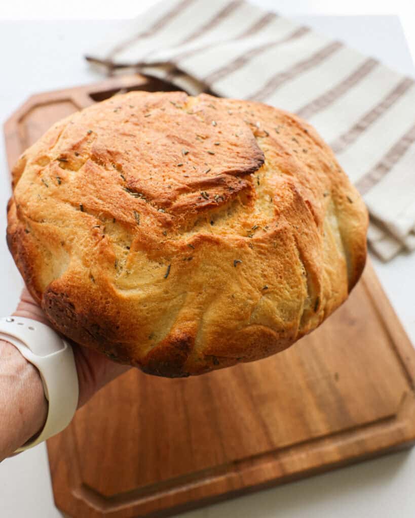 A hand and arm holding up a warm loaf or rosemary potato bread.