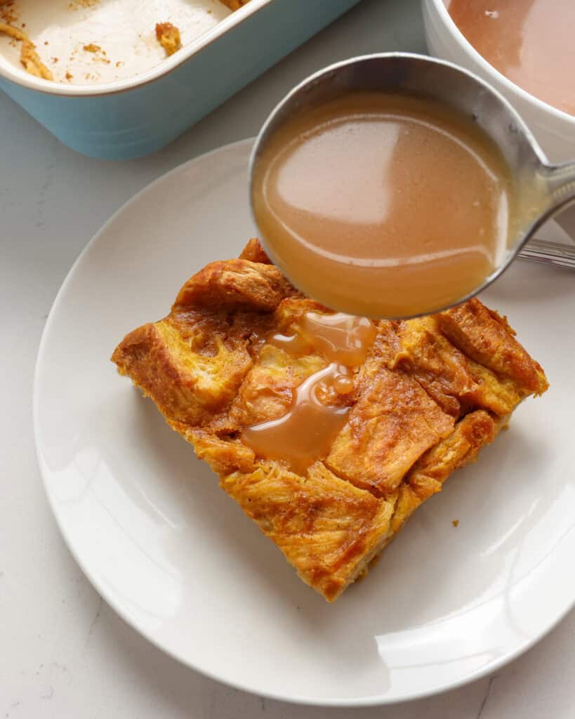 A ladle full of salted caramel sauce drizzled over a piece of pumpkin bread pudding. 