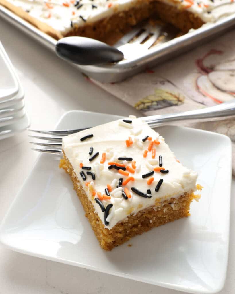 An overhead view of a pumpkin bar on a plate with a fork and the rest of the pan of pumpkin bars in the background.