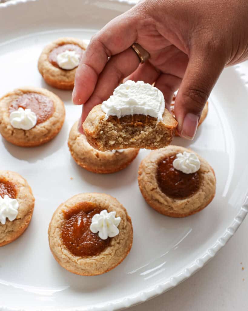 A hand holding a pumpkin pie cookie with a bite out of it.