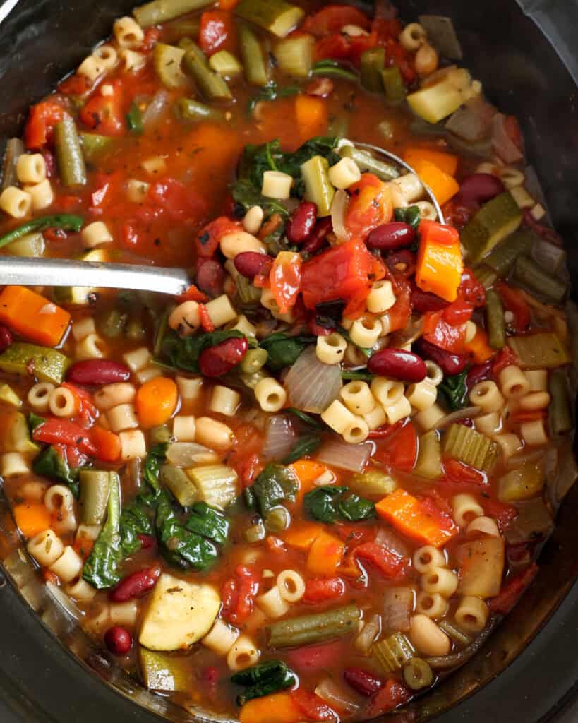 A slow cooker and a ladle full of minestrone soup.